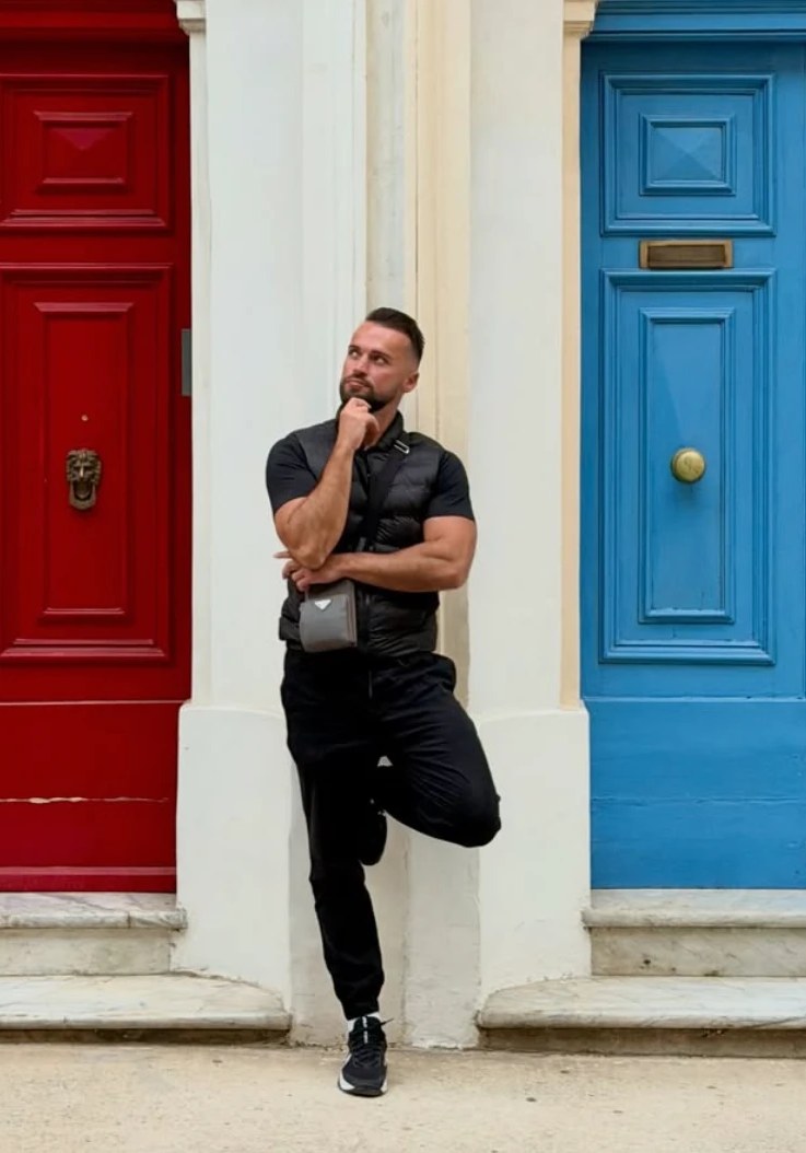 Alex leaning against a doorway between a red and a blue door in Malta